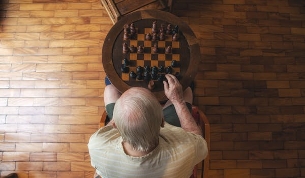 An elderly man playing chess indoors, viewed from above, focuses on strategy and leisure.