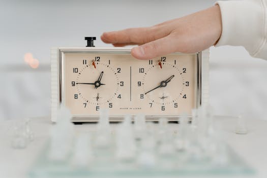 Close-up of a hand adjusting a chess clock during a timed chess game indoors.