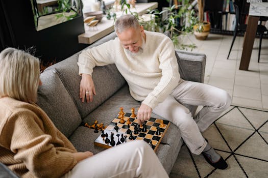 A senior couple playing chess on a cozy sofa, embracing leisure and strategy indoors.